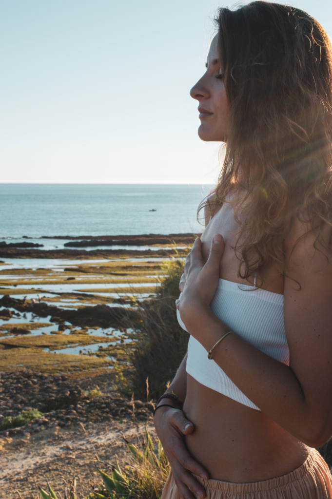 Natalie Montoya with her hand on her chest, eyes lowered, overlooking the sea in Cascais